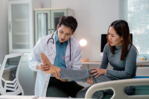 Doctor examining injured foot of female patient sitting on hospital bed