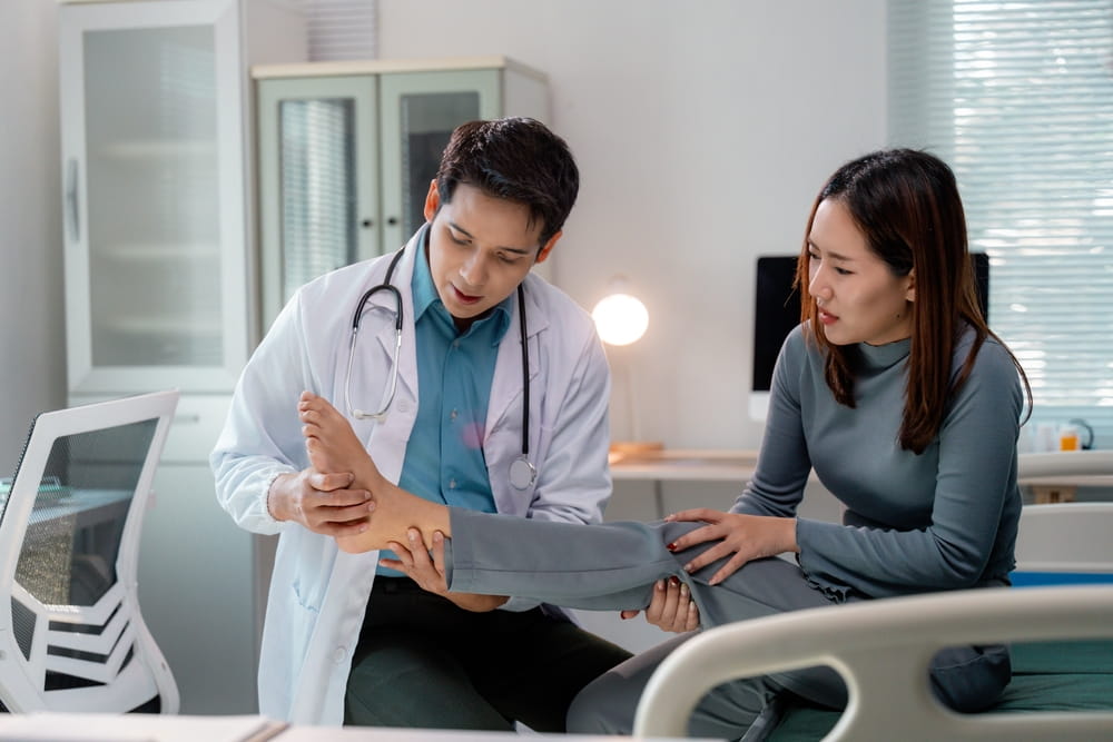 Doctor examining injured foot of female patient sitting on hospital bed